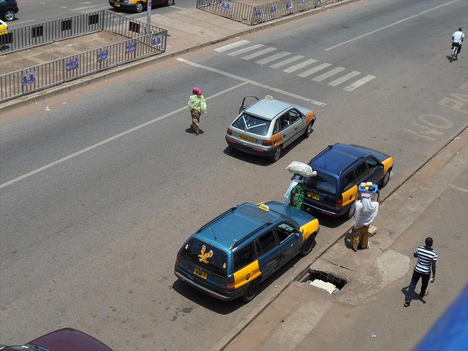 Yellow-and-black taxis picking up passengers on an Accra street, seen from above